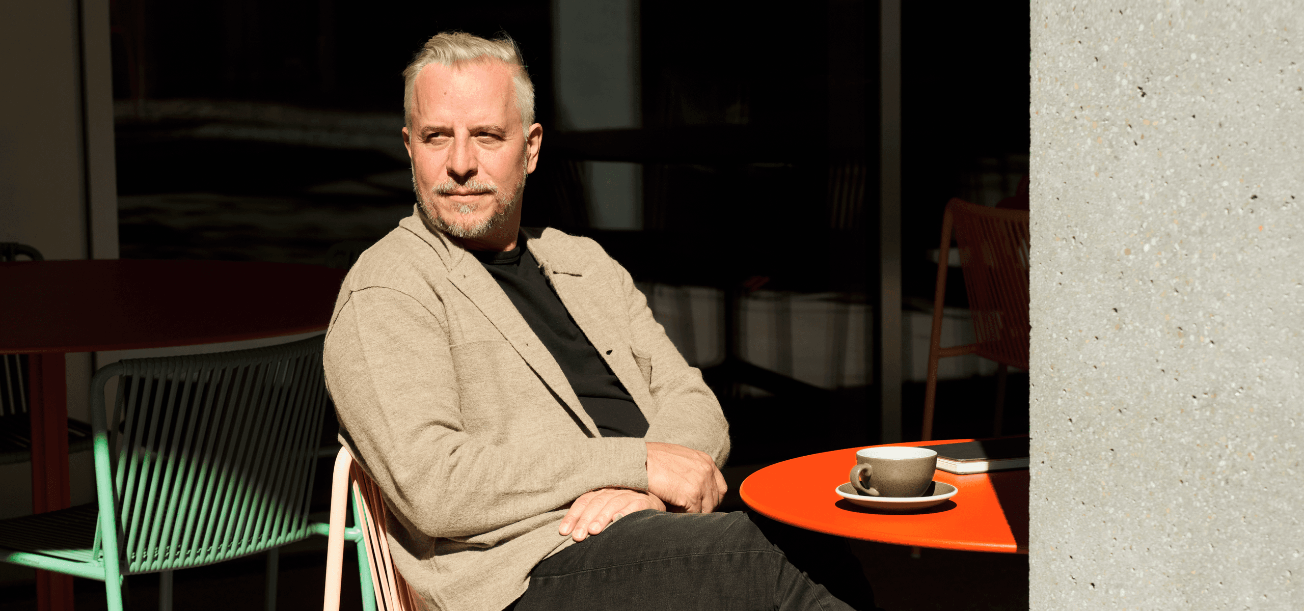 Michael Stuber sitzt an einem roten Tisch im Aussenbereich mit einer Kaffeetasse.