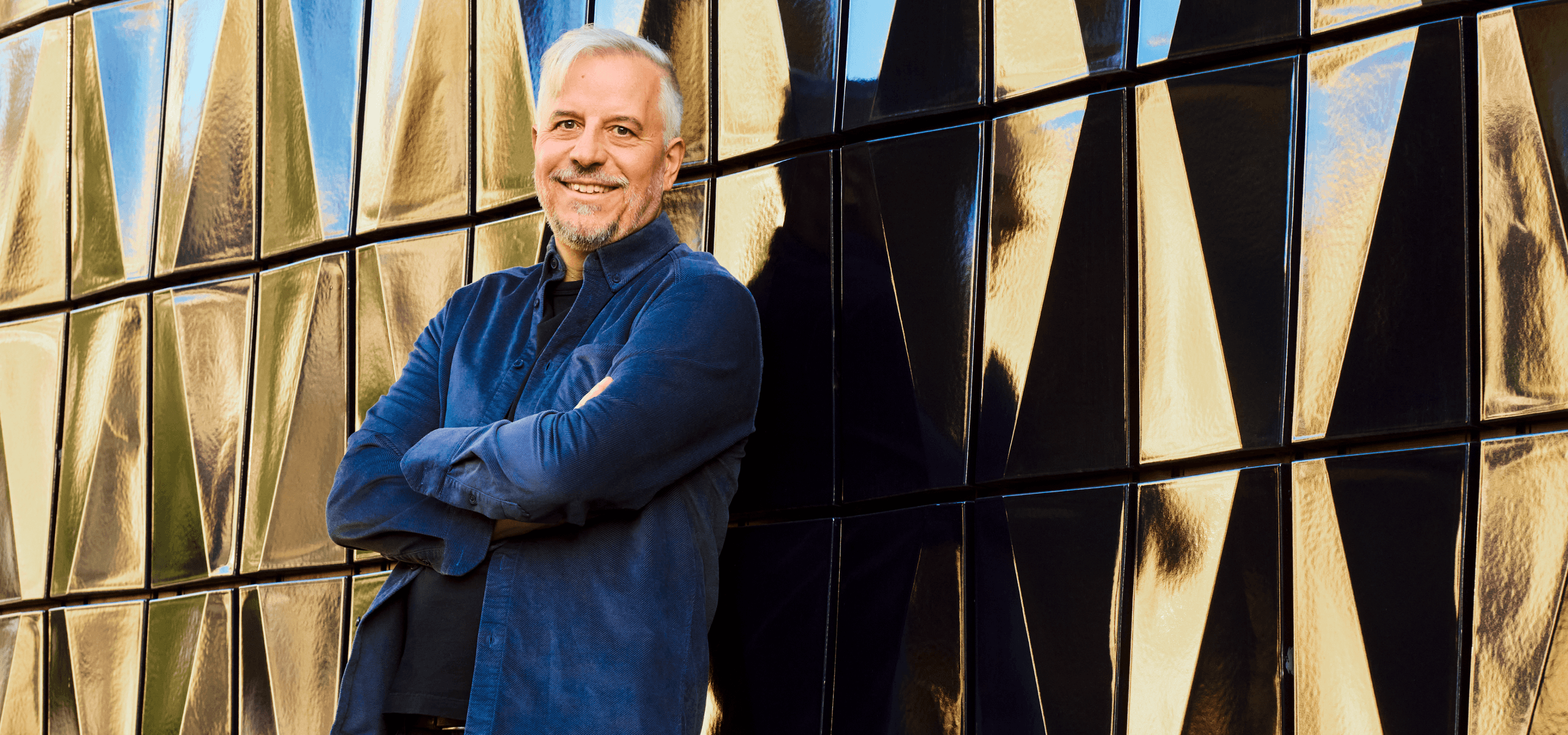 Porträt von Michael Stuber mit verschränkten Armen vor einer geometrischen Wand.